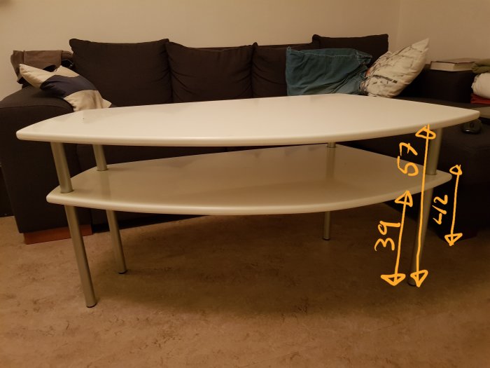 Hemmagjort vitt ovalt bord med måttangivelser framför en soffa.