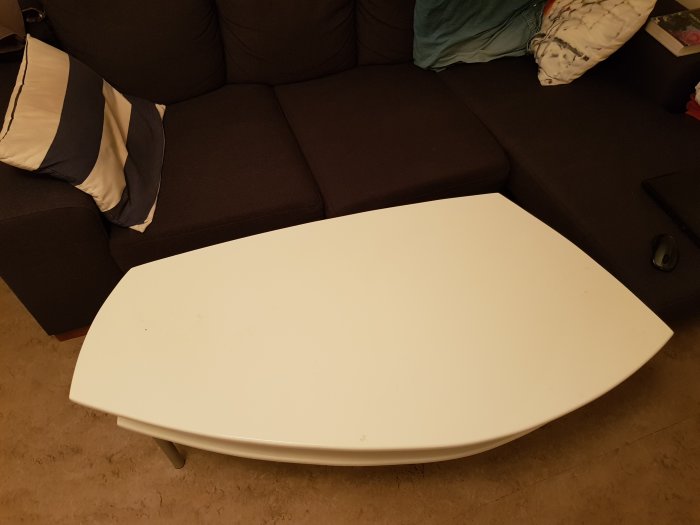 Hemmagjort vitt bord framför en mörk soffa med kuddar, lämpligt för att äta eller använda laptop på.