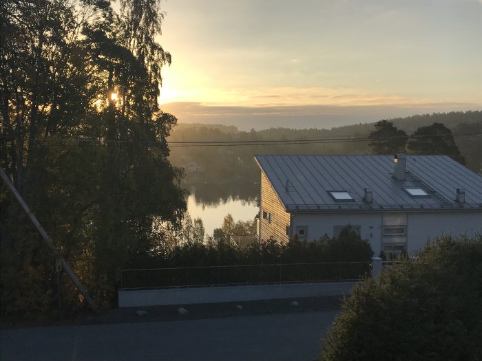 Soluppgång med träd, ett hus och en sjö från en balkong.