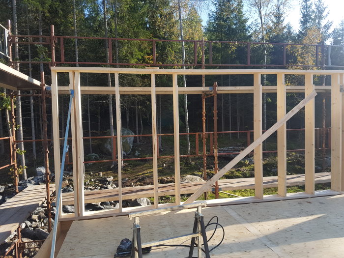 Träreglar i en oavslutad väggkonstruktion på ett byggprojekt med skog i bakgrunden.