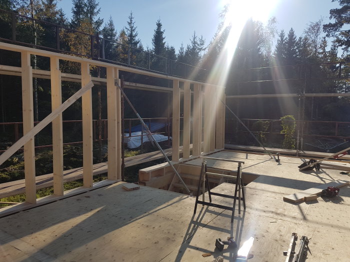 Byggarbetsplats med pågående uppbyggnad av trähusråstomme och verktyg spridda på golvet.