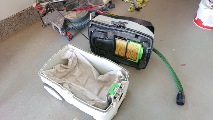 En Festool dammsugare öppnad med uttaget filter och dammpåse i fokus på ett garagegolv.