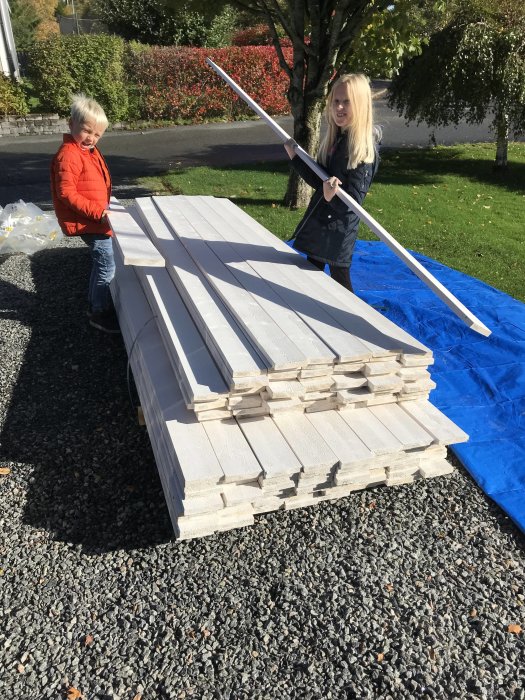 Två personer bär och förbereder en stapel grundmålad fasadpanel utomhus.