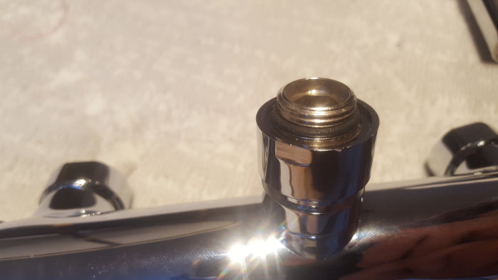 Förkromad duschslangskoppling med invändig gänga på en blank yta.