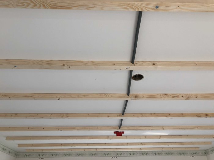 Nyinstallerade träreglar på ett vitmålat tak med synliga elledningar och en utskärning för installationsarbete.