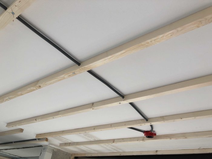 Installation av ljuddämpande undertak med träreglar och mineralullsisolering.