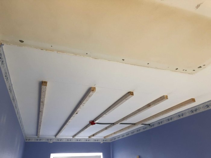 Uppmontering av takstommar för gipsskivor i ett rum med blåa väggar.