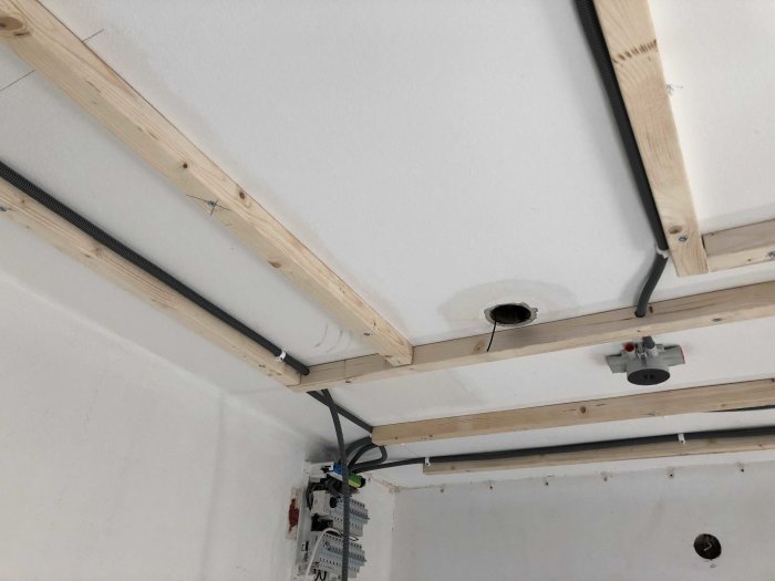 Installation av träreglar på vit takyta med synliga elkablar och en elcentral.