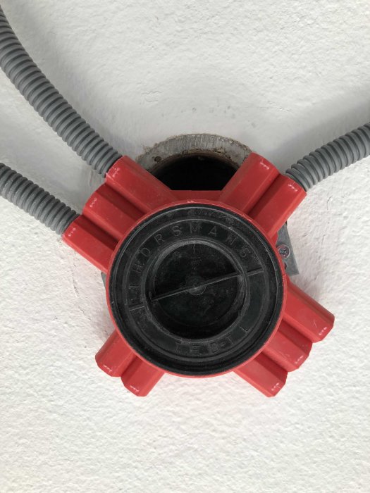 Röd elcentral med grå sladdar i en vitputsad vägg.