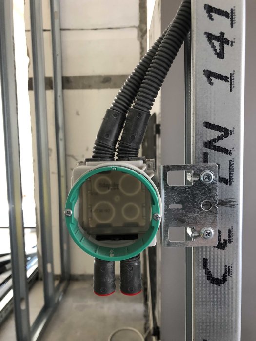 Elinstallation med grön dosa och svart kabelskydd monterat på en metallstomme mot en betongvägg.