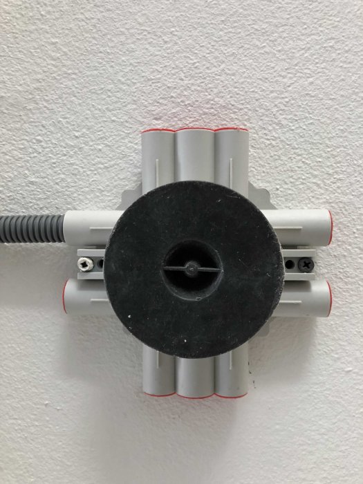 Väggmonterad elinstallation med rör och kabel infäst mot en vit texturerad vägg.