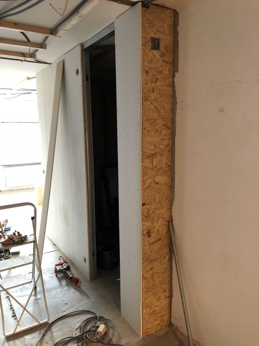 Pågående renovering med öppen gipsvägg och synliga OSB-skivor, verktyg på golvet.