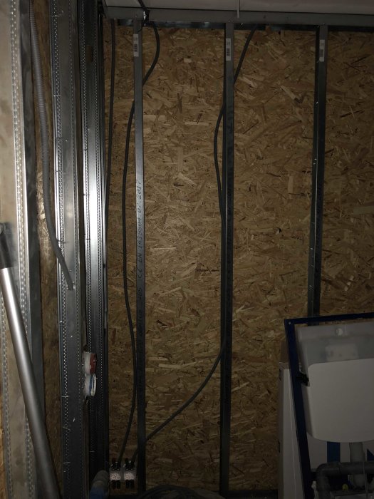 Elledningar monterade längs med metallstolpar mot en OSB-skiva i ett pågående byggprojekt.