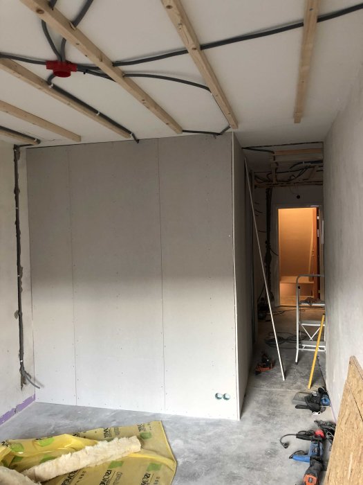 Renoveringsarbete med uppsatta gipsskivor på vägg, synliga takbjälkar och byggmaterial på golvet.