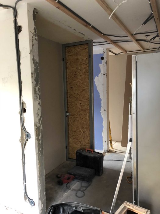 Renoveringsarbete i rum med avskalade väggar, verktyg och en osäkrad dörröppning.