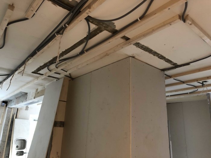 Renoveringsarbete i ett rum med oavslutad gipsskivinstallation och synliga takbjälkar.