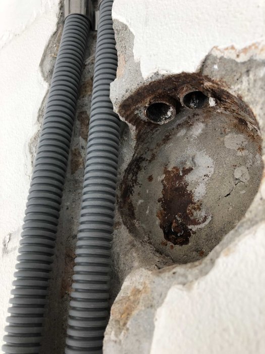 Elrör som går längs en sprucken vägg med synlig rost och betongstruktur.
