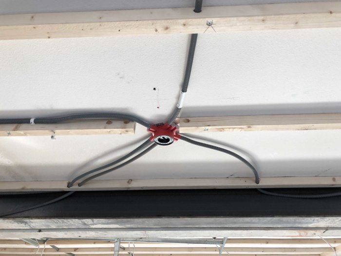 Elledningar fastsatta vid taket med en röd kabelsamling och flexibla skyddsrör mot en vit bakgrund.