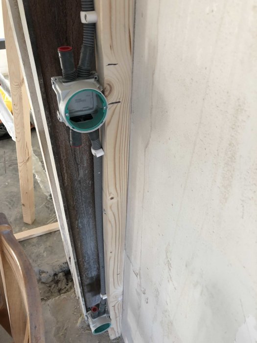 Vattenmätare monterad på vägg med rör och elektrisk kabel installerade i en byggmiljö.