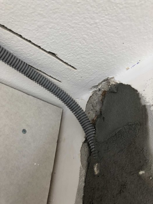 Spricka i ett vitt tak nära grå betong och ett svart genomföringsrör.