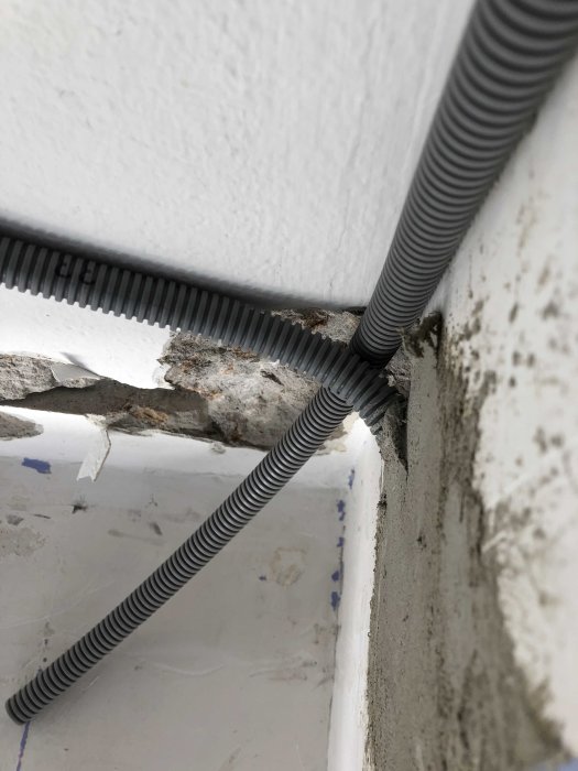 Grovt genomfört elinstallation med flexibla svarta rör som träs genom ojämna hål i en vit vägg.