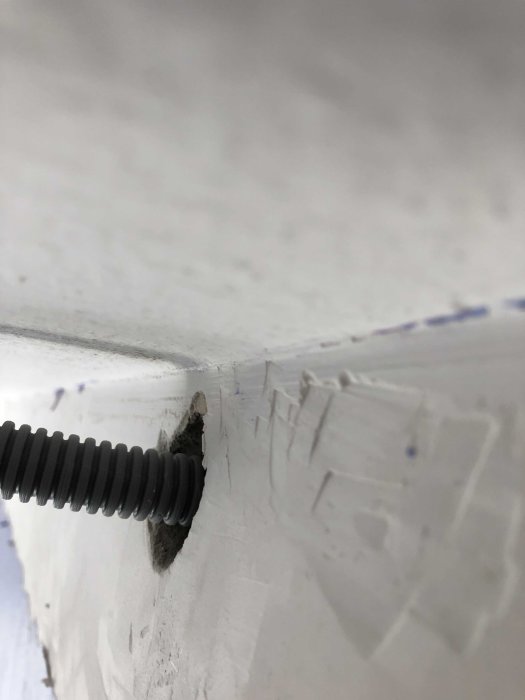 Närbild av en grå kabelskyddsrör som passerar genom en vit vägg med spår av byggdamm och märken.