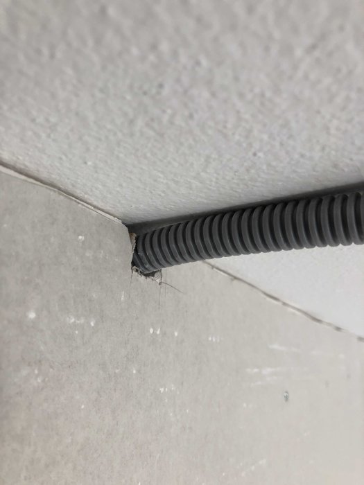 Elledning i flexibel svart skyddsslang som passerar genom ett hål i ett vitt hörn av en vägg.