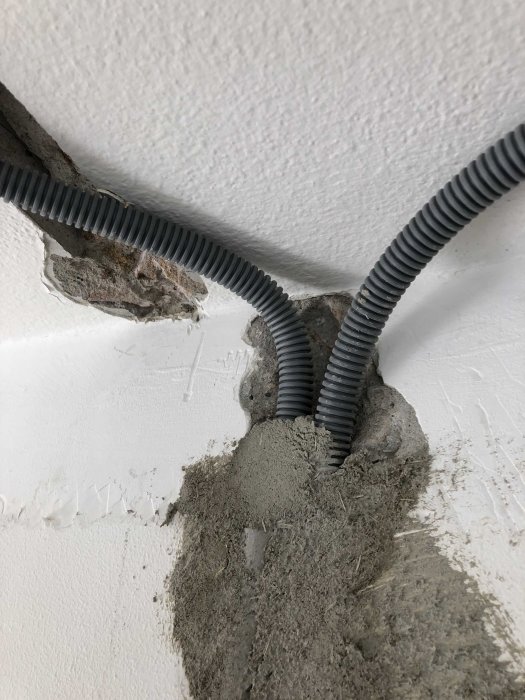 Elledningar i flexibel rörskyddning som framträder från en vägg med spackel och hål.