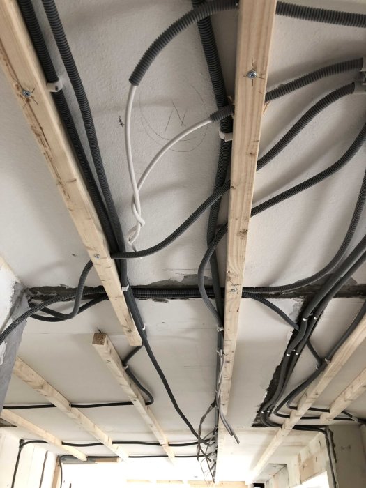 Installation av eldragning med kablar och elrör som är fästa i takbjälkar under renovering.