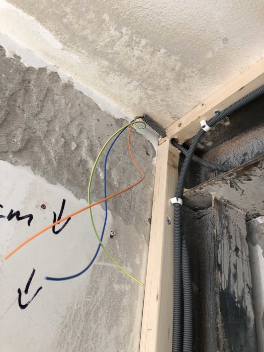 Elektriska kablar i färgerna röd, grön, gul och blå som sticker ut från en väggtätning i en byggnadsstomme.