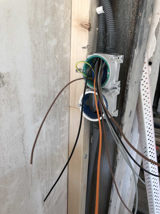 Oavslutad elinstallation med öppen eldosa och utstickande kablar vid ett byggprojekt.