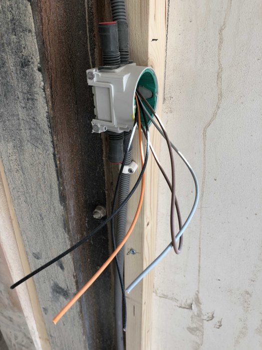 Eluttag under installation med synliga kablar och rör på en vägg.