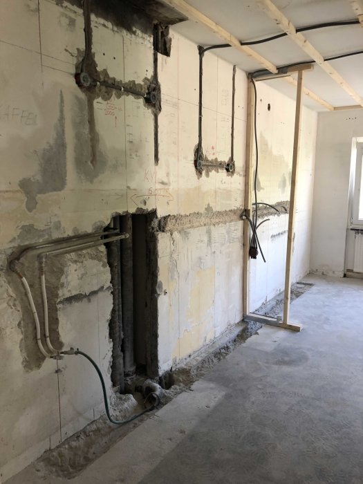 Renoveringsarbete pågår med exponerade rör och elinstallationer längs en avskalad vägg.