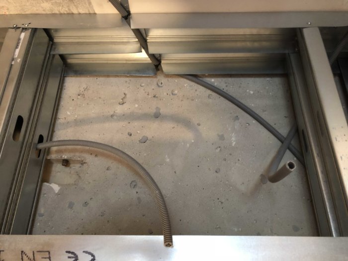 Översiktsbild av ett betonggolv med genomföringar och elinstallationer under konstruktion.