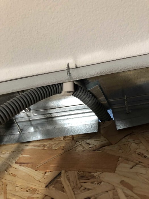 En närbild på installation av en luftkanal och elslang nära taket, med synligt OSB-golv i förgrunden.
