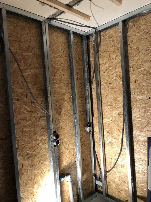 Interiör av en vägg under konstruktion med exponerade metallstuds och OSB-skivor.