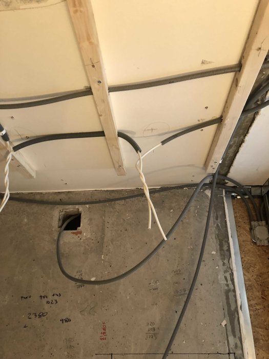 Öppet elsystem och kablar längs en vägg under konstruktion, med markeringar på betonggolvet.
