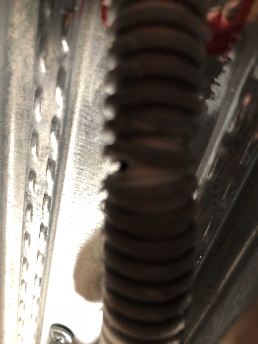 Närbild på skadad flexibel elrörskoppling med synlig tråd och metallprofil.