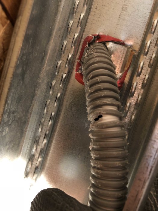 Elektrisk kabelskydd genomtränger metallprofil med röd tätning.