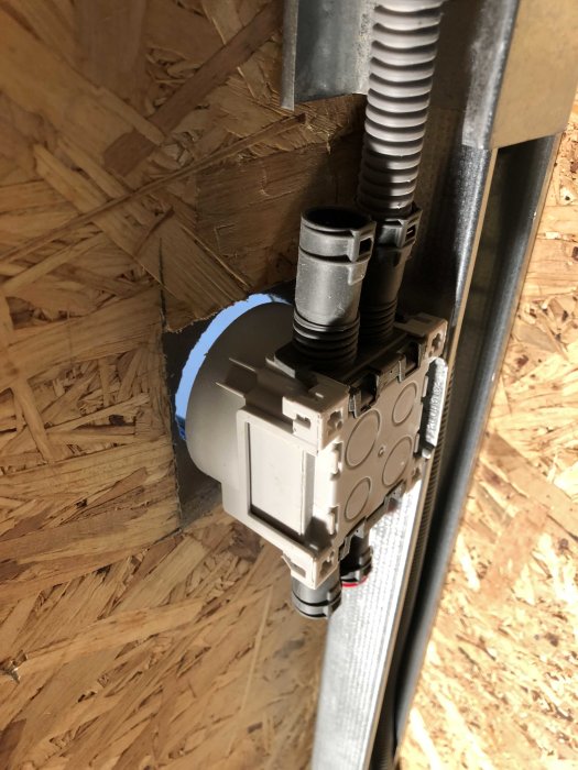 Elinstallation med rör som går genom en OSB-skiva, fastsatt vid en väggprofil.