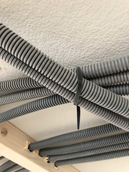 Grå kabelförvaringsrör ordnade parallellt och upphängda med buntband på en träbalk.