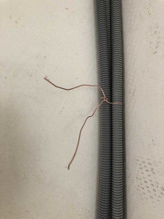 Två gråa elektriska kabelförvaringsrör längs en vit vägg, med en utstickande koppartråd.