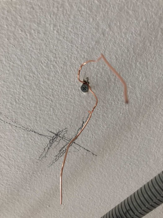 Kopparkabel som sticker ut från en vägg där en skruv är delvis iskruvad.