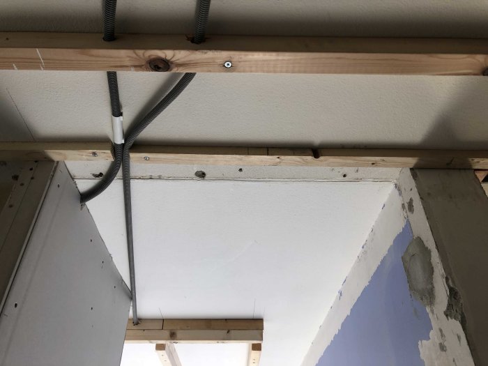 Installation av elledningar och kablar på en träregel vid ett tak och en vit gipsskivvägg under konstruktion.