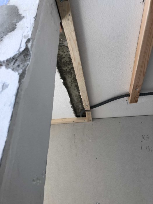 Delvis installerad gipsvägg med synlig träregel och elektrisk kabel, intill oputsat betongområde.