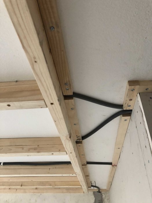 Träreglage för innertak med synliga skruvar och elektrisk kabelrör i hörnet.