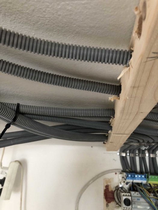 Elektriska kablar i flexibla rör som är osäkert fästa i taket bredvid en öppen elcentral.