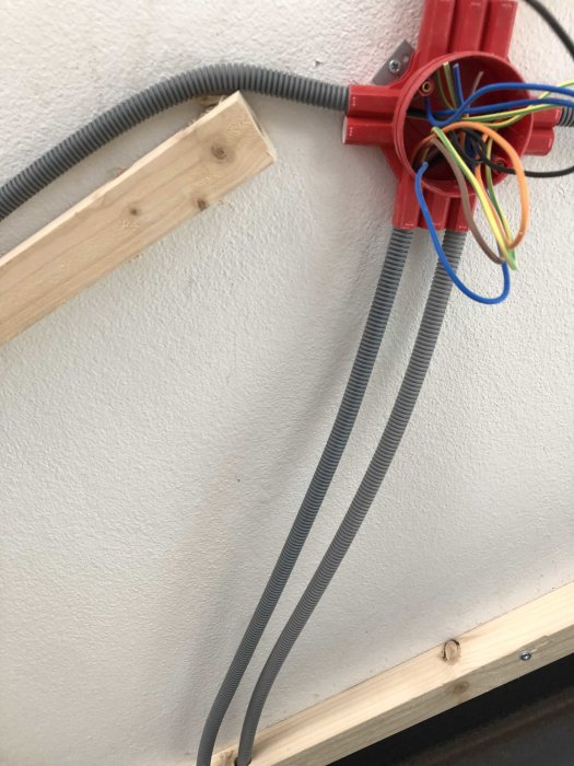 Elledningar i flexibel slang monterade på träregel och röd dosa med öppen kabeldragning.