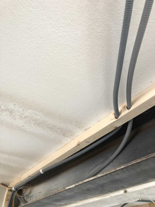 Fuktfläckar på en innertak i närheten av träreglar med genomförande elkablar och flexibla rör.