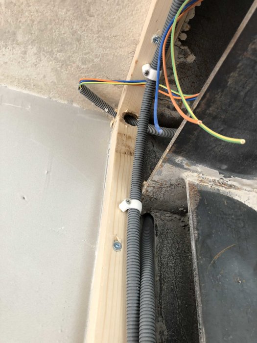 Elinstallation i vägg med synliga kablar och flexibla rör fastsatta på en träregel.